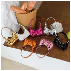 Seven colorful mini bow handbags in metallic finish displayed on a wooden table setup