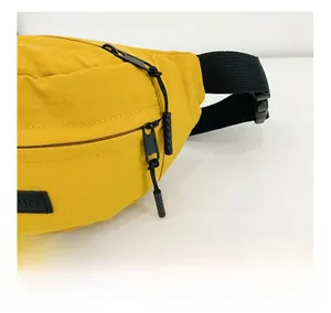 Dettaglio della doppia cerniera nera e del tessuto in nylon stropicciato del marsupio giallo