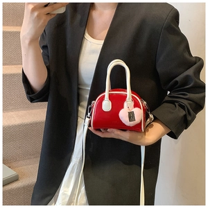 Mini red shell bag with white handles and a pink plush heart charm shown in hand