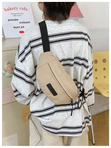 Dettaglio della borsa da petto in nylon beige con tracolla nera e toppa del marchio