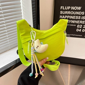 Detail of neon green nylon half-moon bag featuring a plush moon charm and adjustable strap