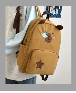 Détail d'un sac à dos jaune avec oreilles d'ours et écusson étoile porté par un modèle
