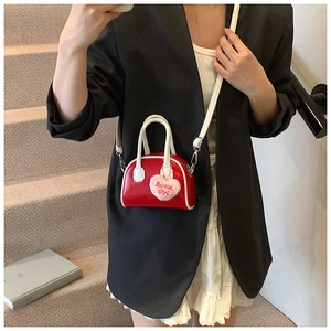 Detail of red glossy mini shell bag with pink plush heart pendant on model