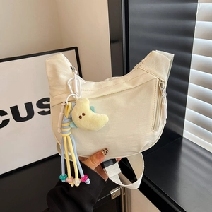 Detail of a beige crescent nylon crossbody bag with a cute yellow moon plush pendant