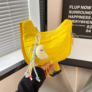 Detail view of yellow nylon crescent sling bag with a white plush cloud charm accessory