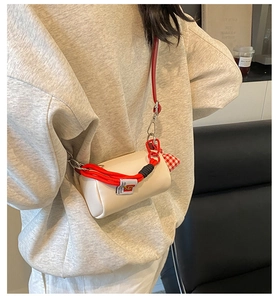 Modella che indossa una borsa a cilindro crema con manico a nodo rosso e tracolla vivace