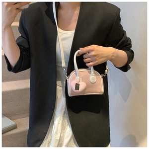 Detailed view of kids' pink shell-shaped crossbody bag with a plush heart charm and white handle