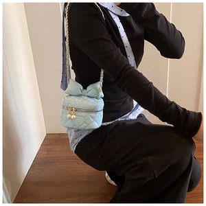 Close-up of light blue quilted crossbody bag with oversized bow and pearl zipper charms