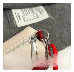 Dettaglio macro della cerniera argentata e rifiniture rosse su borsa a cilindro beige