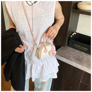Detail view of mini cream and pink shell bag featuring a plush Barbie Girl heart charm