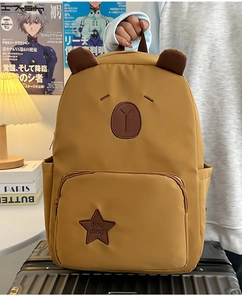 Détail d'un sac à dos moutarde avec oreilles d'ours et broderie d'étoiles sur une valise