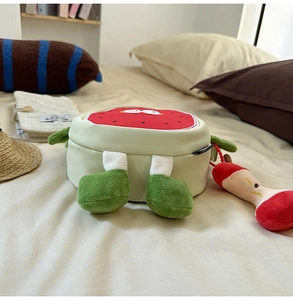 Detailed view of watermelon plush crossbody bag with cute apple core charm on bed