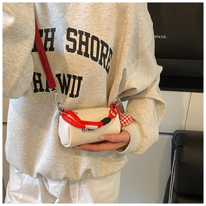 Dettaglio della mini borsa cilindrica bianco avorio con tracolla rossa e ciondolo a cuore
