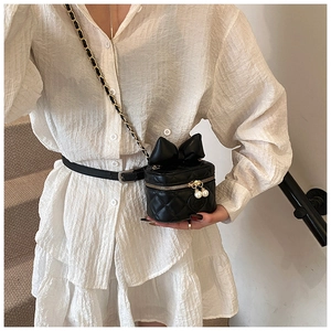 Close-up of black quilted mini bag with bow and pearl zipper details on crossbody chain
