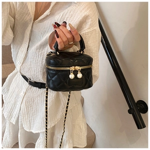 Detailed view of black quilted mini vanity bag with gold zippers and pearl accents