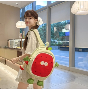 Close-up of a cute watermelon plush backpack with cartoon face and red mushroom charm