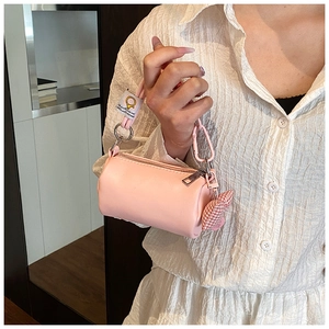 Dettaglio mini borsa cilindrica rosa con manico intrecciato e ciondolo a cuore