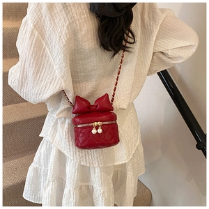 Close-up of a red quilted mini crossbody bag with bow detail and gold chain strap