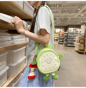 Detail of cute green fruit plush crossbody bag with a cartoon face and apple core charm