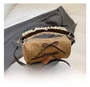 Detalle de bolso cilíndrico de ante marrón con lunares, lazos y asa decorada con encaje