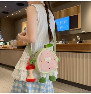 Detail of cute green fruit crossbody bag with pink face design and red apple plush charm