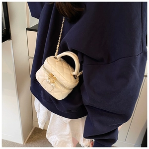 Détail d'un mini sac matelassé crème avec breloque perle et chaîne dorée sur modèle