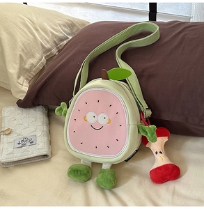 Detail of cute guava crossbody bag with soft plush limbs and apple charm on a bed