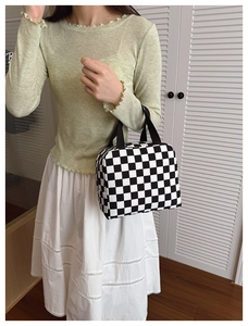 Detail of checkered lunch bag with black strap handles and zip closure held by a model