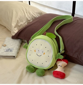 Detail of green fruit plush crossbody bag featuring cartoon face and apple core charm