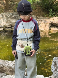 Outdoor shot of a mini green nylon neck pouch for kids with adjustable strap and carabiner