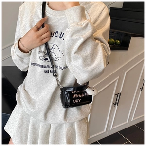 Detail of a black glossy cylinder crossbody bag with pink lettering and white fur charm