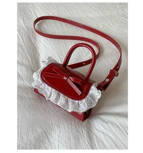 Macro detail of red mini crossbody bag with white lace trim and bow on shiny leather