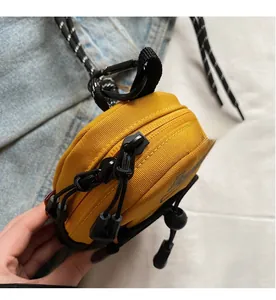 Detail view of mini yellow crossbody bag showing smooth double zippers and black plastic hook