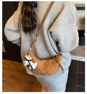 Close-up of brown suede croissant bag with knotted strap and cute puppy charm detail