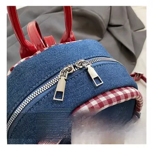 Detailed close-up of blue denim backpack showing silver metal zippers and red plaid trim