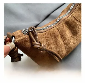 Detail of brown suede crescent bag featuring silver metal zipper and knotted strap