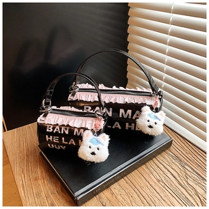 Detail of black cylindrical crossbody bags with pink lace trim and puppy pendants