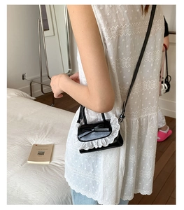 Mini black PU crossbody bag with white lace trim and bow detail shown on shoulder