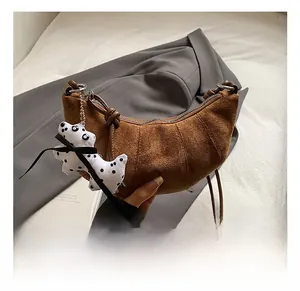 Detail of brown matte suede croissant bag with zipper and plush puppy charm accessory