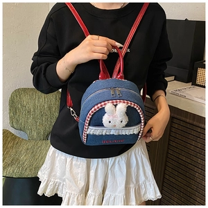 Close-up of denim backpack featuring a plush bunny head, lace trim and red strap detail