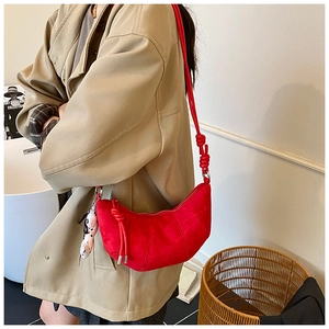 Detail view of red suede crescent bag featuring woven strap and playful polka dot charm