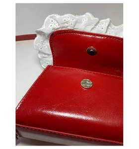 Detail of red patent leather mini bag with silver magnetic buckle and white lace trim