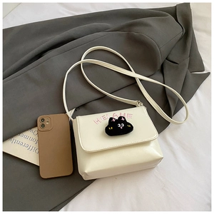 Detail of a beige PU leather crossbody bag featuring a cute black cat plush patch