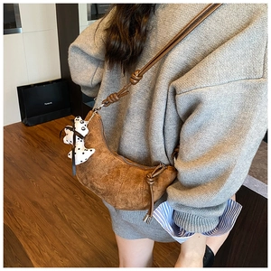 Detail of a brown suede croissant bag for kids featuring a cute white dog charm