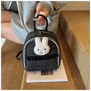 Detail of a mini black denim backpack with a plush bunny head and lace ruffles