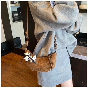 Close-up of brown suede crescent bag with knot strap detail and polka dot puppy charm