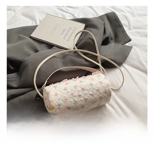 Close-up of cylindrical white fabric crossbody bag with pink bow print and lace details