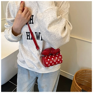 Detail of red polka dot cylinder bag with decorative bow and brand engraving