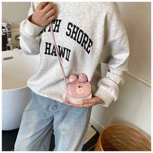 Détail du sac à bandoulière rose avec nœud 3D et broderie pomme porté par un modèle