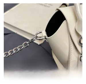 Detail of silver chain strap and D-ring buckle on cream patent leather mini handbag